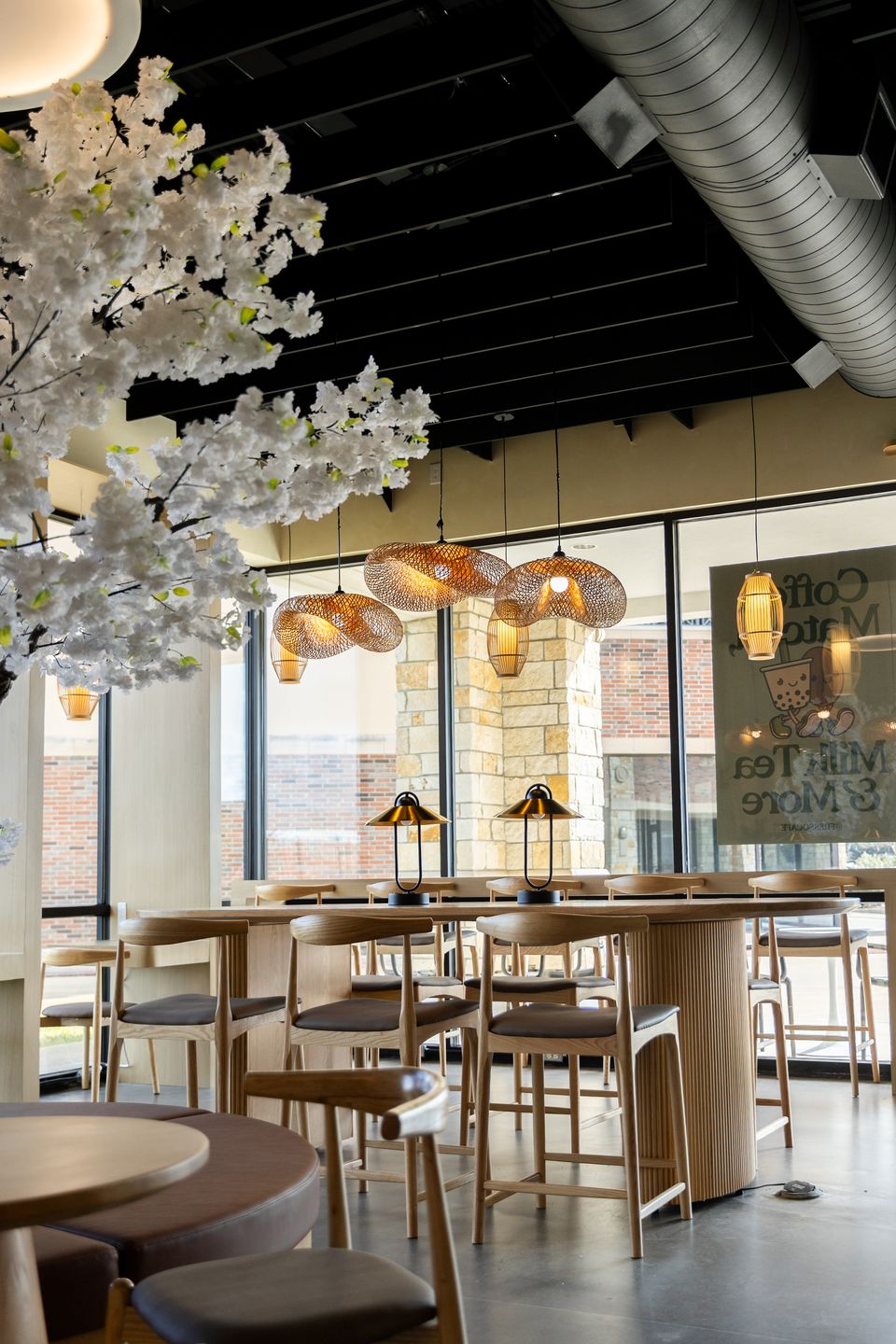 The main room at Fresso Cafe: a white blossom tree, rattan pendant lights and a long oak table by the windows